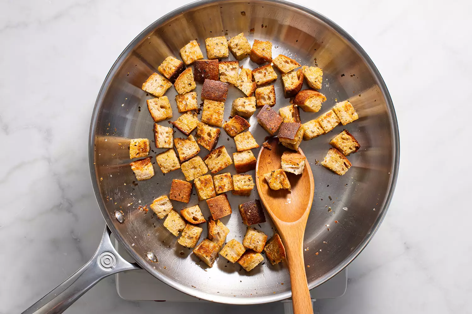 Cubes de pain dans une poêle sur un brûleur, avec une cuillère en bois