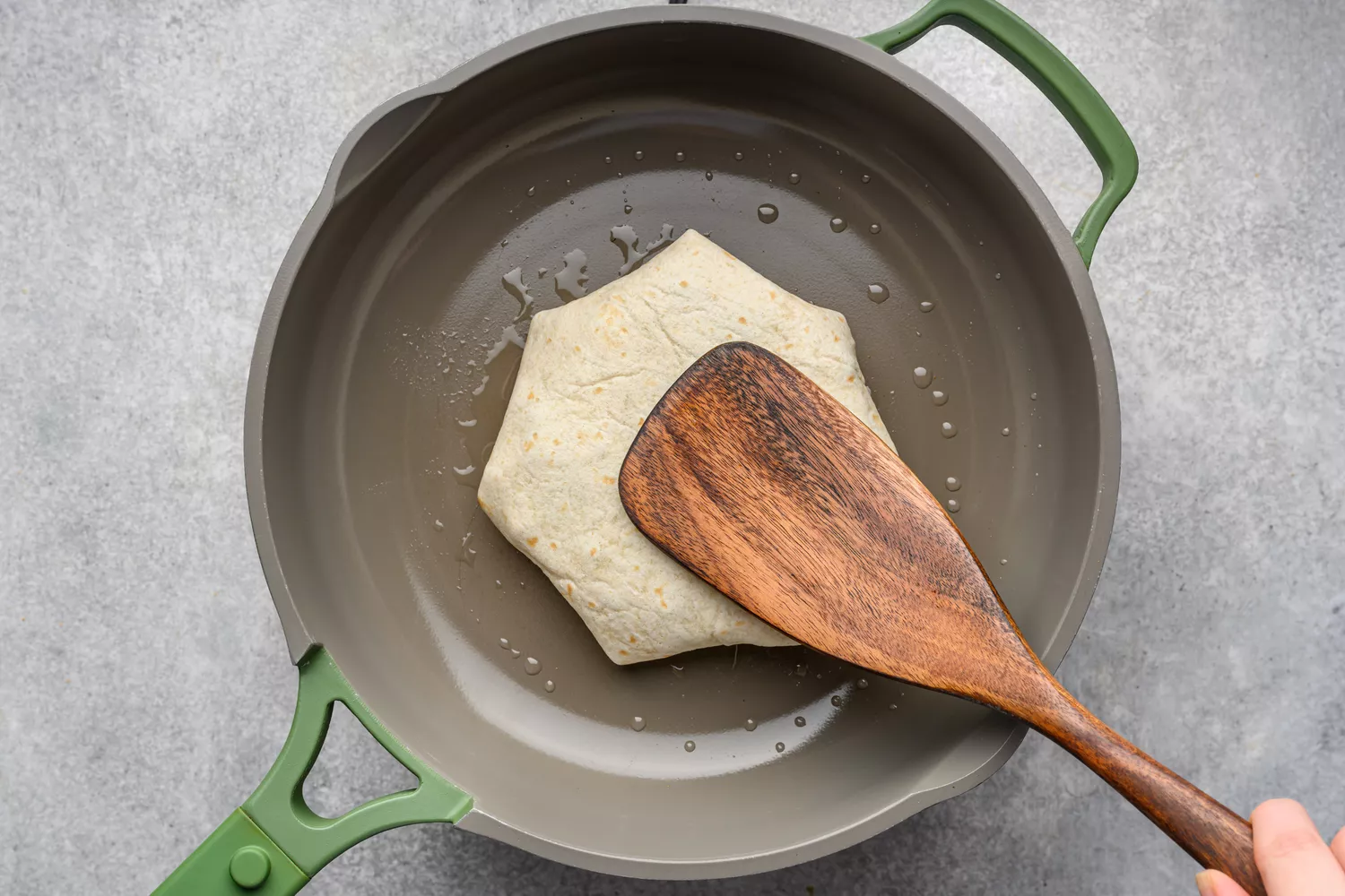 Une cuillère en bois appuyant sur un Crunchwrap Supreme dans une poêle antiadhésive huilée