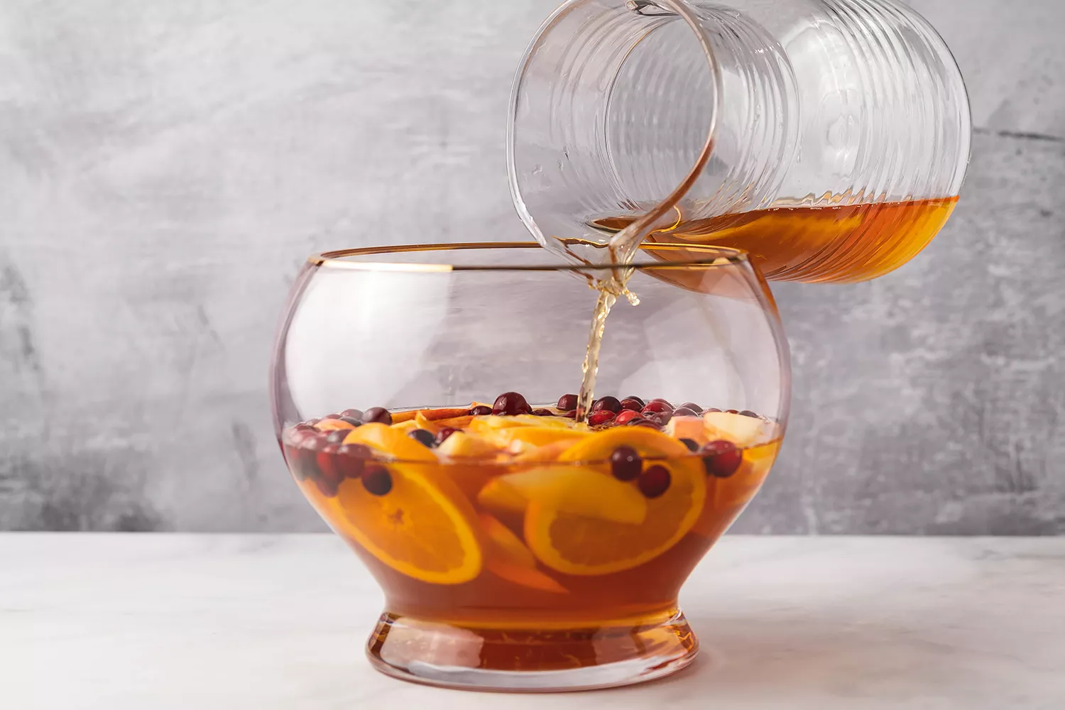 Cidre, fruits, et jus de fruits ajoutés à un bol à punch pour le punch de Thanksgiving