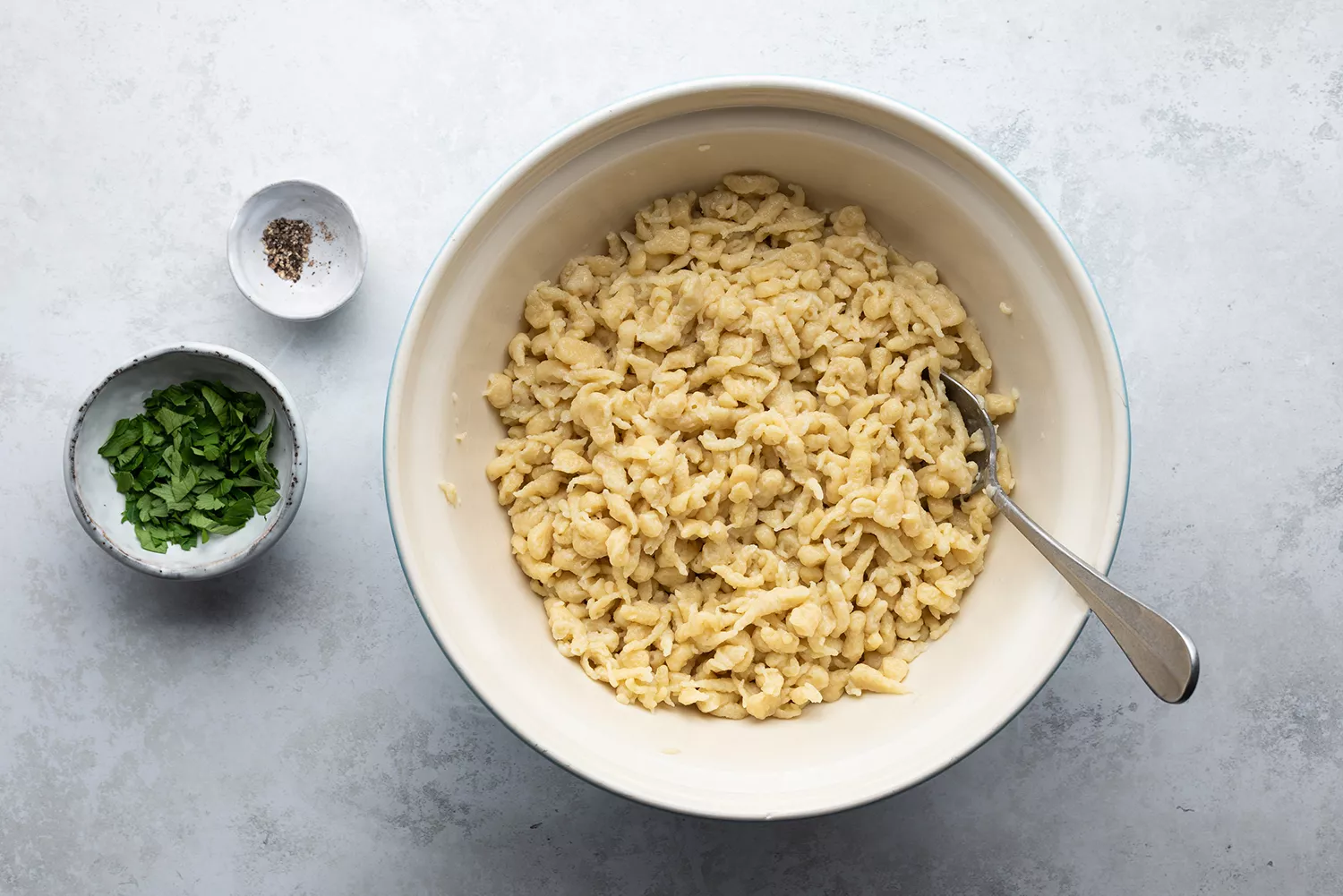 Spaetzle dans un bol, herbes et poivre noir dans de petits bols