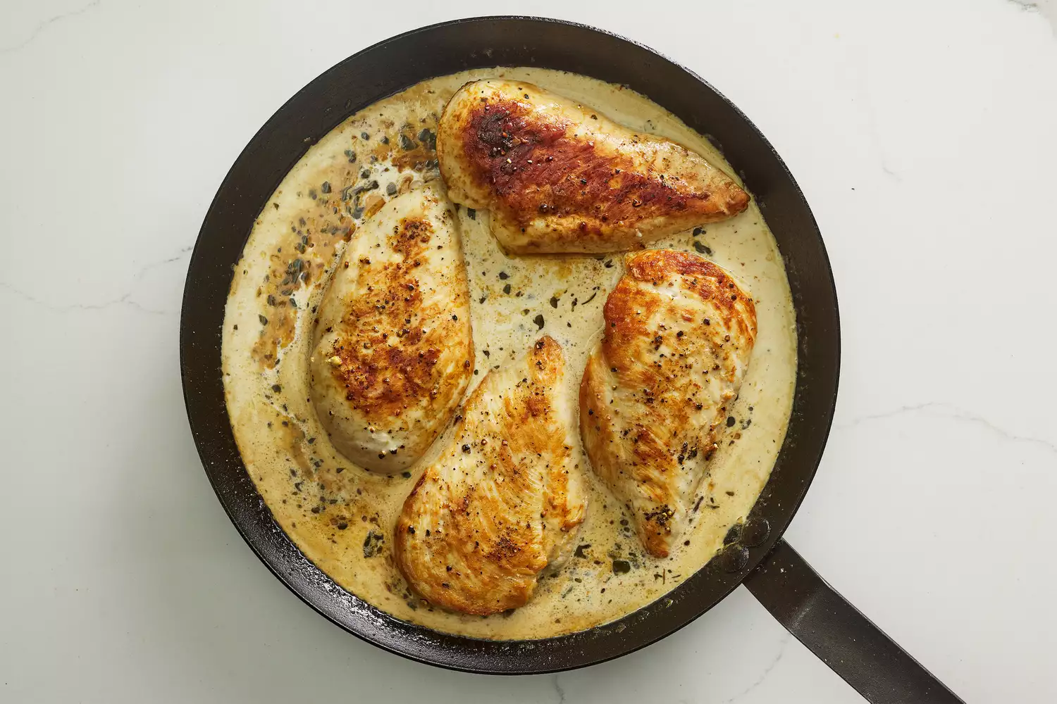 A skillet with four chicken breasts cooking in a creamy dijon sauce