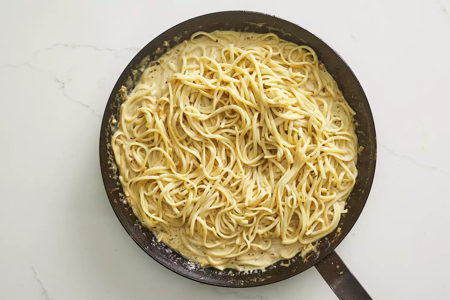 A skillet with cooked fettuccini tossed in a creamy dijon-parmesan sauce