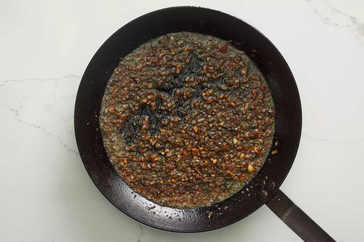 A skillet with shallots, garlic, and herbs cooking in butter