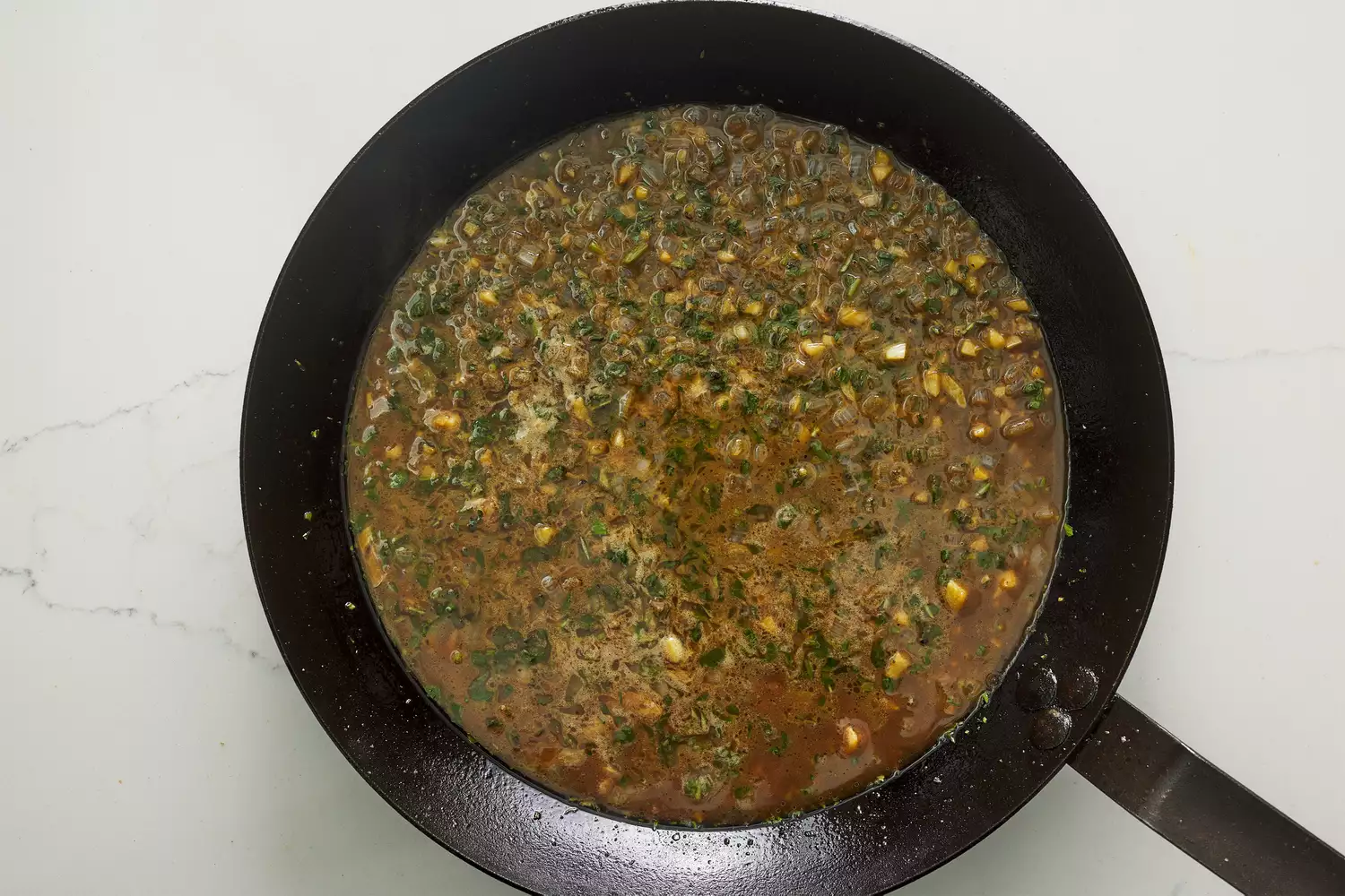 A skillet with garlic, shallot, and herbs cooking in white wine